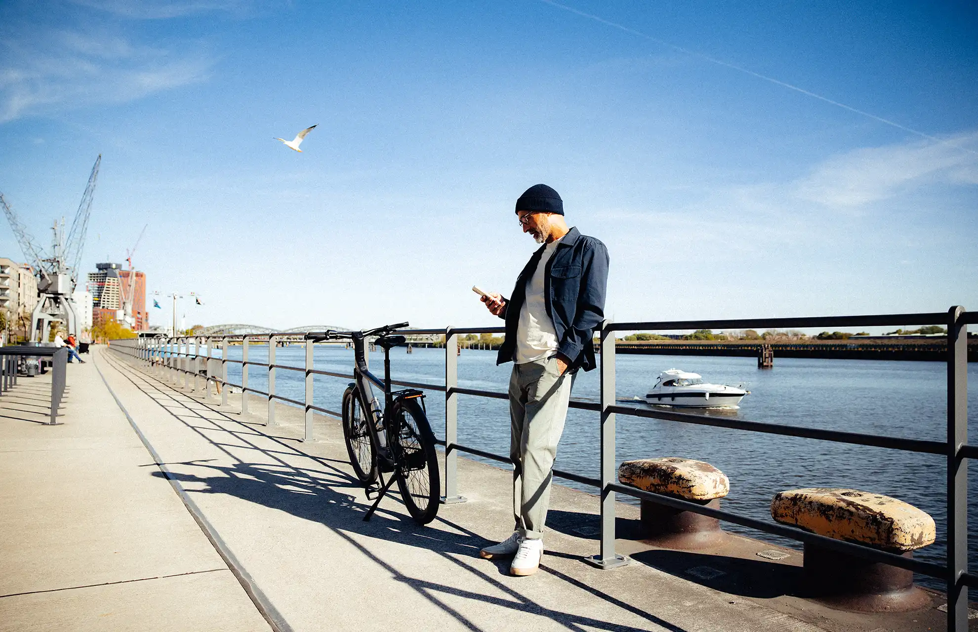 Mann steht mit Dienstrad am Hafenkanal und schaut aufs Handy